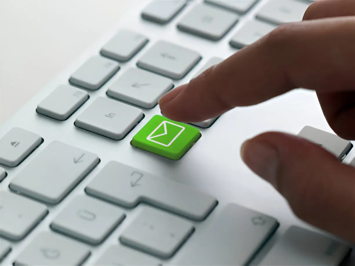 Doigt appuyant sur une touche de clavier verte avec l'icône d'une enveloppe (e-mail), symbolisant la messagerie professionnelle.